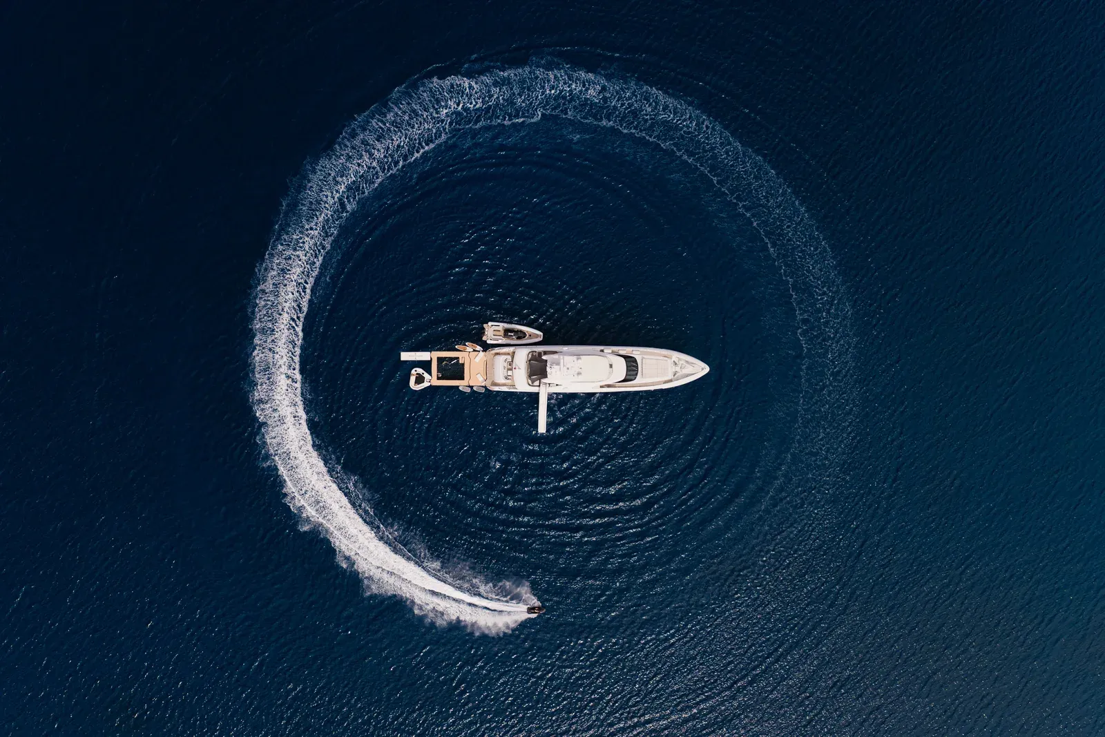 Tender carving a circle on flat blue water, aerial
